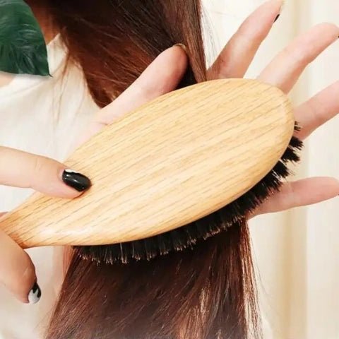 Jeune femme de côté qui brosse ses longs cheveux roux avec la brosse à poil de sanglier naturel