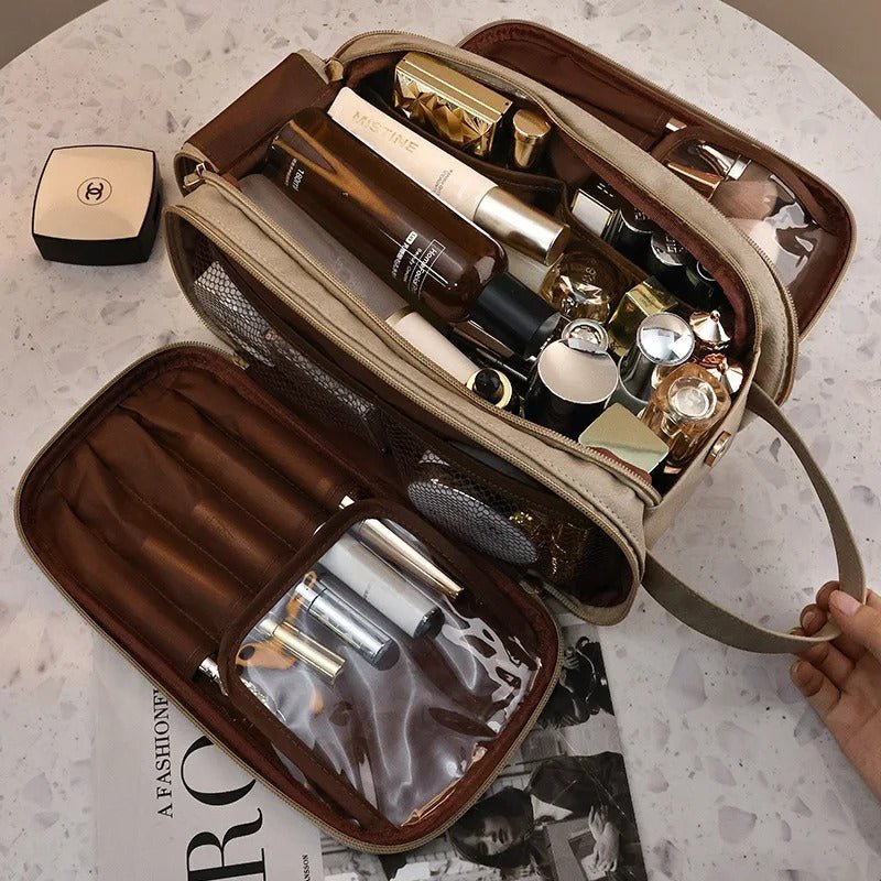 Trousse de toilette multi compartiments couleur beige avec articles de maquillage et de beauté à l'intérieur déposée ouverte sur une table en marbre blanc
