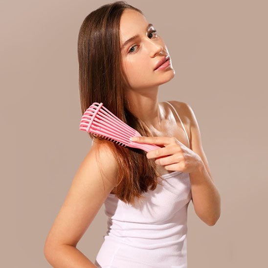 Jeune femme longs cheveux roux se brossant les cheveux avec la brosse à cheveux bouclés pour cheveux épais de couleur rose