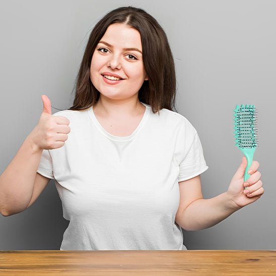 Jeune femme aux longs cheveux bruns qui tient la brosse cheveux bouclés verte dans sa main gauche et fait un pouce levé de son autre main