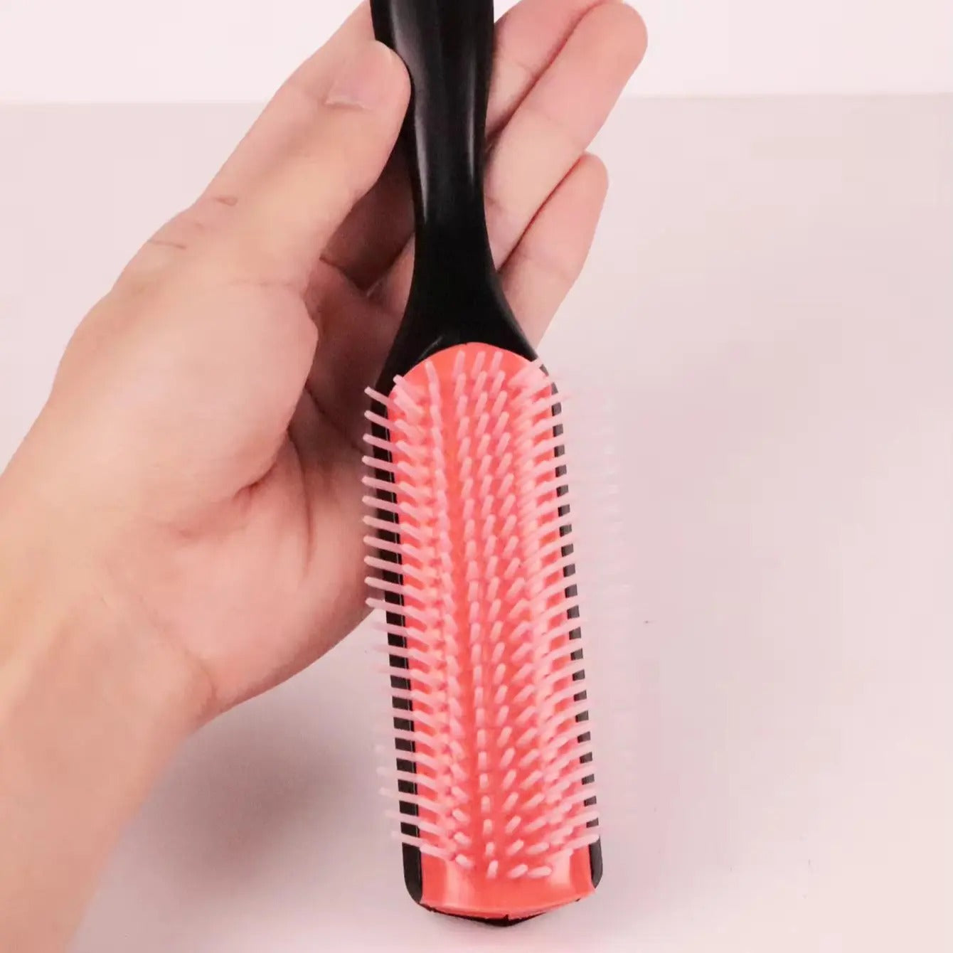 une main tenant la brosse pour cheveux bouclés couleur rouge