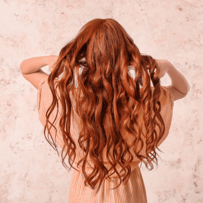 jeune femme aux longs cheveux bouclés roux installée de dos