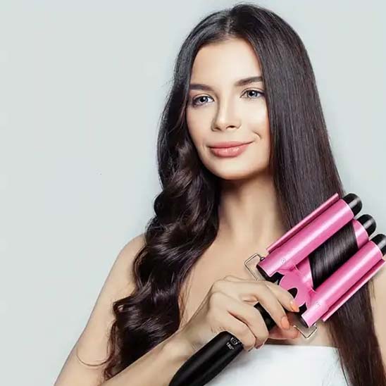 Jeune femme souriante aux longs cheveux foncés qui boucle ses cheveux avec le boucleur rose 