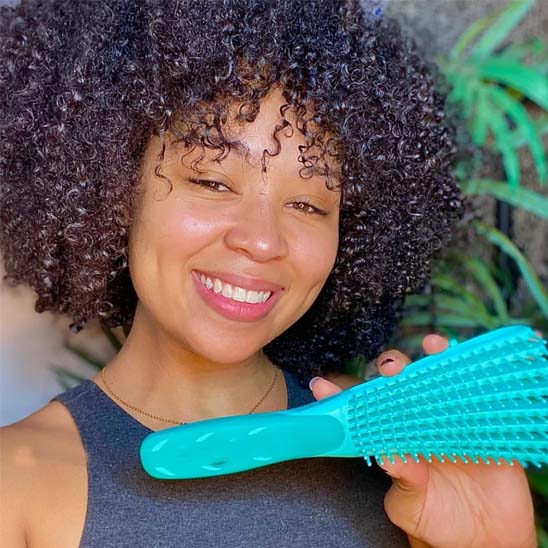 Jeune femme type afro montrant souriante la brosse à cheveux bouclés pour cheveux épais de couleur verte 