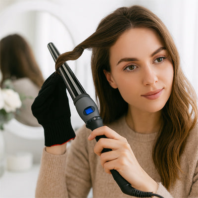 Jeune femme qui boucle ses cheveux avec le fer bouclant.  Elle porte également un gant thermique protecteur