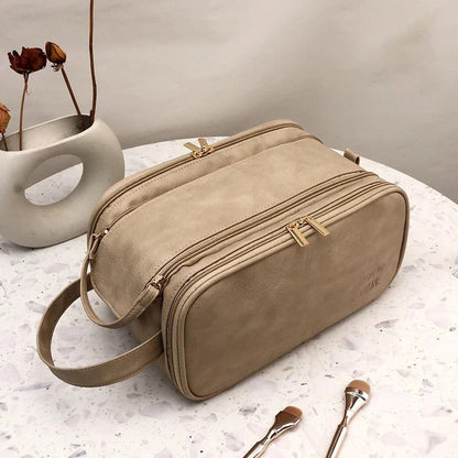 Trousse de toilette multi compartiments  couleur camel déposée sur une table en  marbre blanc