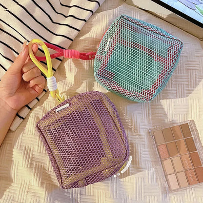 une main qui tient le cordon des trousses de toilette couleur violet et cyan