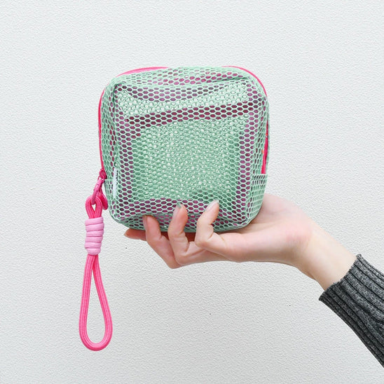 Une main de femme qui tient la trousse de toilette couleur cyan afin d'en apprécier toutes les caractéristiques