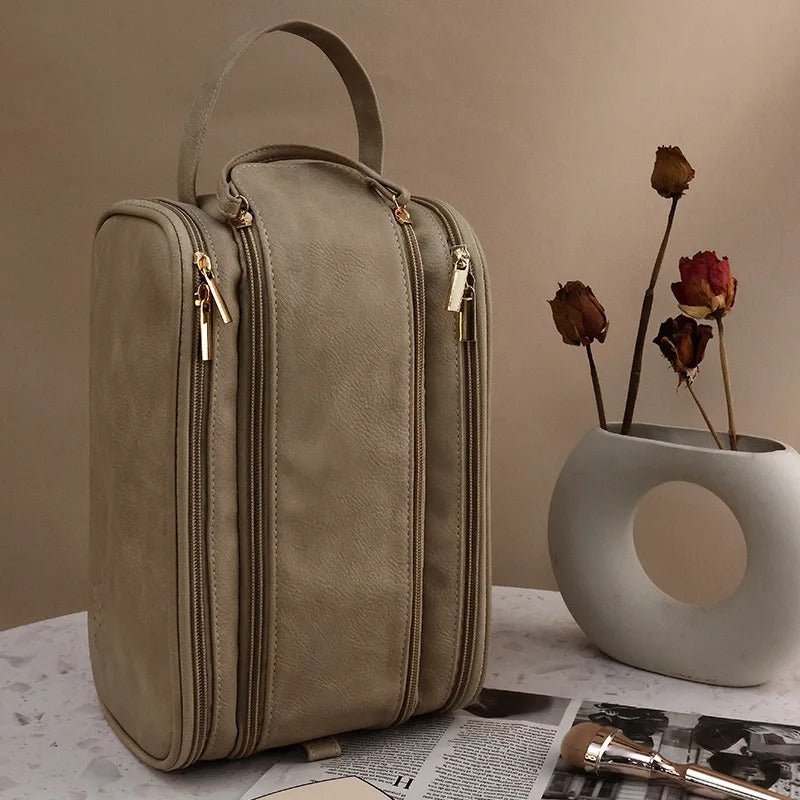 Trousse de toilette multi compartiments couleur camel placée debout sur une table en  marbre blanc