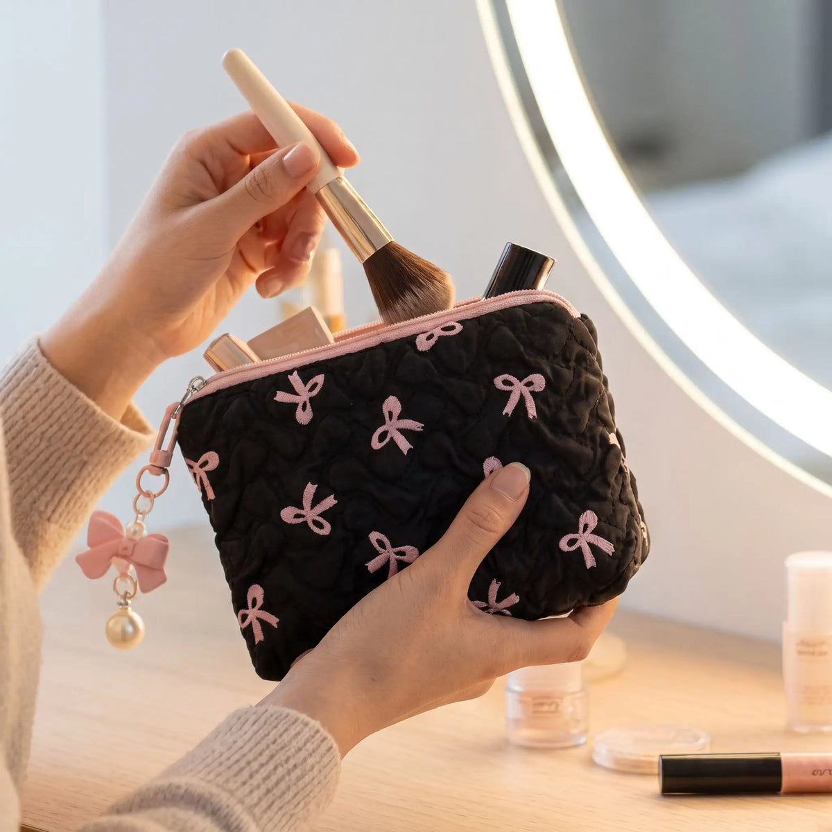 trousse de toilette noire et rose une main place des articles de maquillage dans la trousse 