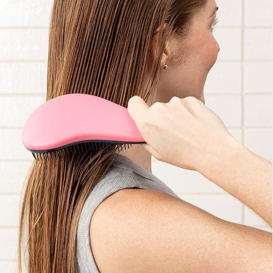 Jeune femme avec longs cheveux châtains roux qui se brosse les cheveux avec la brosse à cheveux anti noeud de couleur rose 