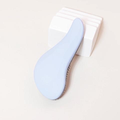 Brosse à cheveux couleur bleue posée sur un plan crème et appuyée sur un bloc décoratif blanc