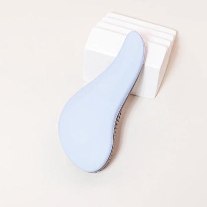 Brosse à cheveux couleur bleue posée sur un plan crème et appuyée sur un bloc décoratif blanc