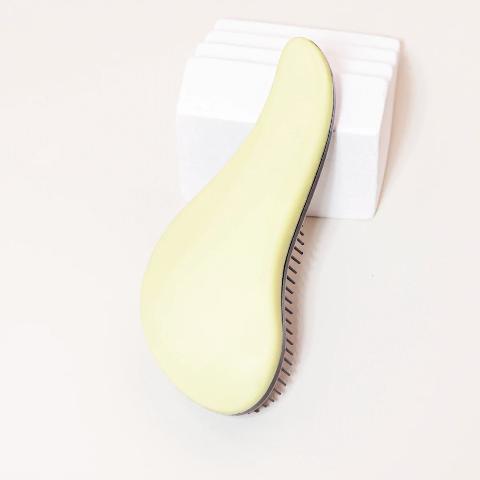 Brosse à cheveux couleur jaune posée sur un plan crème et appuyée sur un bloc décoratif blanc