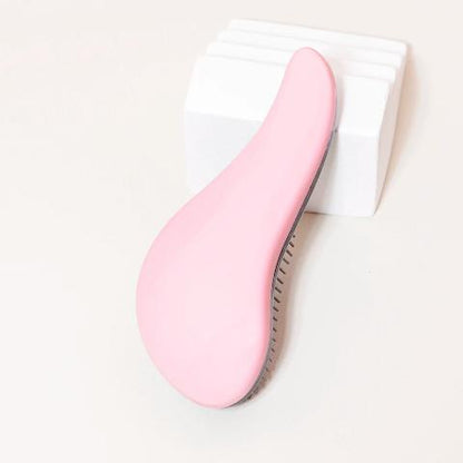 Brosse à cheveux rose posée sur un plan crème et appuyée sur un bloc décoratif blanc