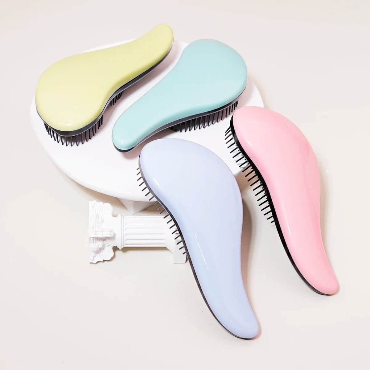 Brosse à cheveux 4 couleurs offertes posées sur un plan crème et présentoir rond blanc 