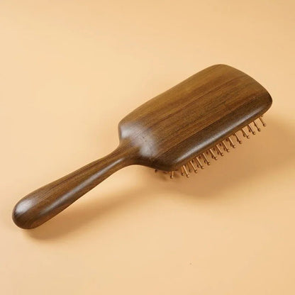 Brosse à cheveux en bois de santal format carré posée de face sur un plan jaune beige