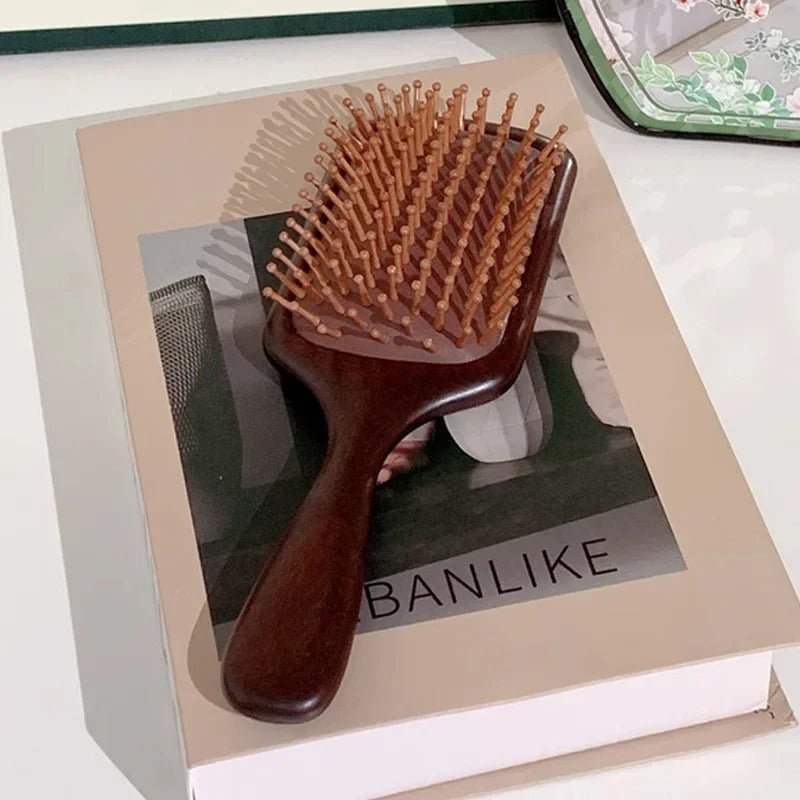 Brosse à cheveux en bois de santal format carré posé sur un livre 