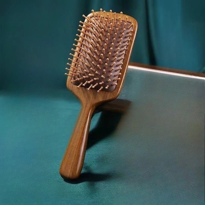 Brosse à cheveux en bois de santal format carré posé sur un plan vert 