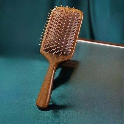 Brosse à cheveux en bois de santal format carré posé sur un plan vert 