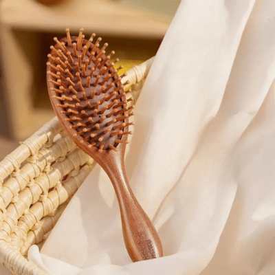 brosse à cheveux en bois de santal posé sur un drap crème dans un panier en osier 