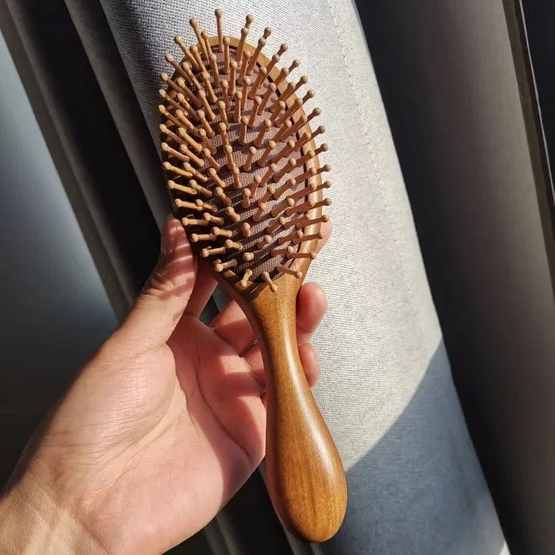 Une main qui tient la brosse à cheveux en bois de santal de forme ronde 