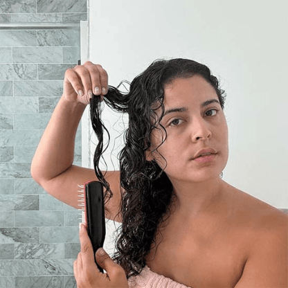 Jeune femme aux cheveux longs mouillés bruns qui se coiffe avec la brosse à cheveux bouclés