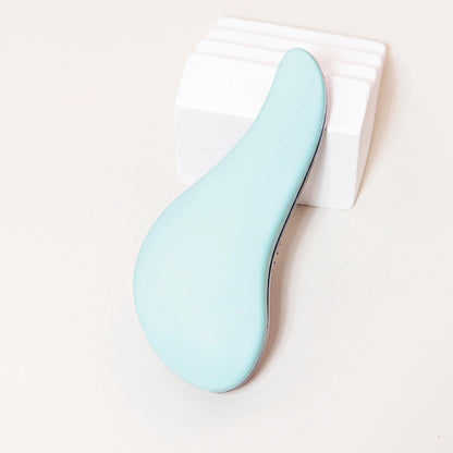 Brosse à cheveux de couleur verte posée sur un plan crème et appuyée sur un bloc décoratif blanc
