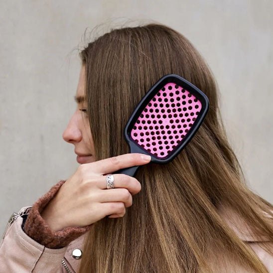 Jeune femme de profil longs cheveux châtains qui brosse ses cheveux avec la brosse à cheveux démêlante de couleur rose