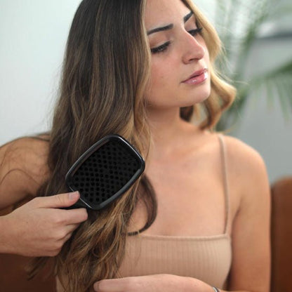 Jeune femme aux longs cheveux châtains qui démêle ses cheveux avec la brosse à cheveux noire 