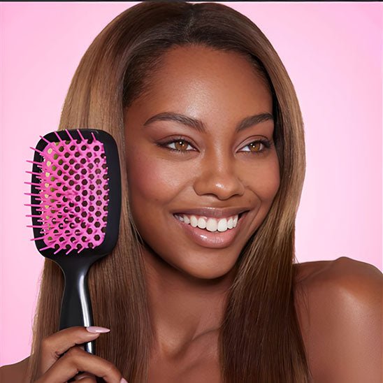 Jeune femme souriante aux longs cheveux châtains qui tient la brosse à cheveux démêlante 