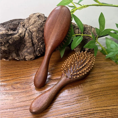 Brosse à cheveux en bois de santal de forme ronde appuyée sur une pièce de bois et une autre posée sur un plan en bois