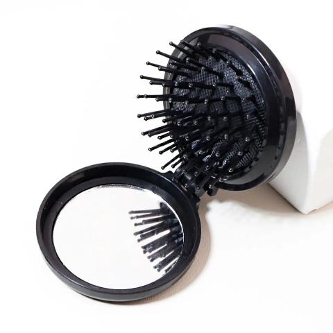 Brosse a cheveux couleur noire poils noirs posée sur un plan blanc