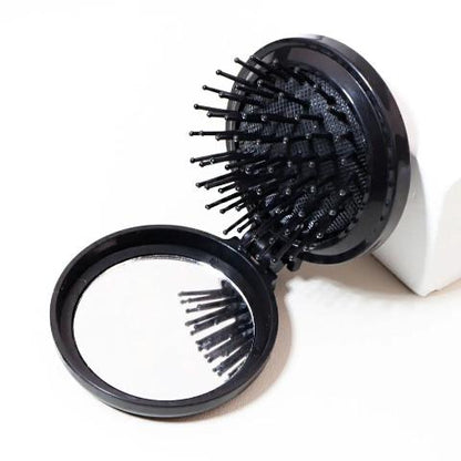 Brosse a cheveux couleur noire poils noirs posée sur un plan blanc
