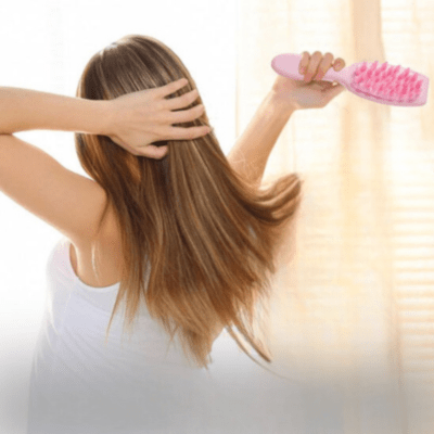 Jeune femme positionnée de dos avec longs cheveux châtains qui se brosse les cheveux avec la brosse à cheveux massage 