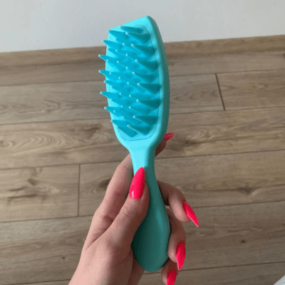 une main aux ongles vernis qui tient la brosse a cheveux massage de couleur bleue 