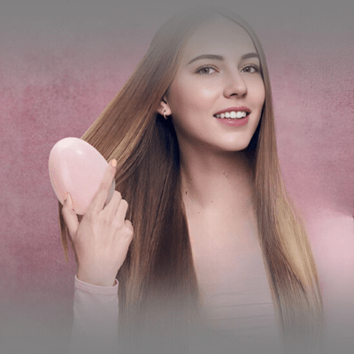 Jeune femme avec longs cheveux châtains qui se brosse les cheveux avec la brosse à cheveux mini oeuf rose 