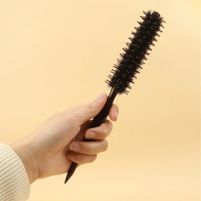 Une main de jeune femme qui tient la brosse à poils de sanglier format moyen