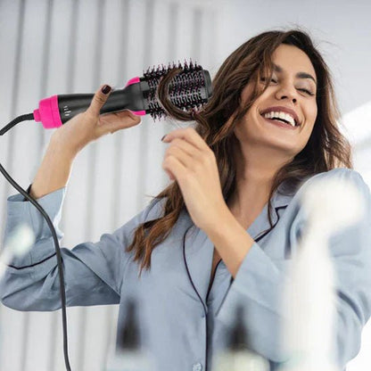 Jeune femme cheveux longs bruns qui se coiffe avec la brosse chauffante à air chaud de couleur noir et rose