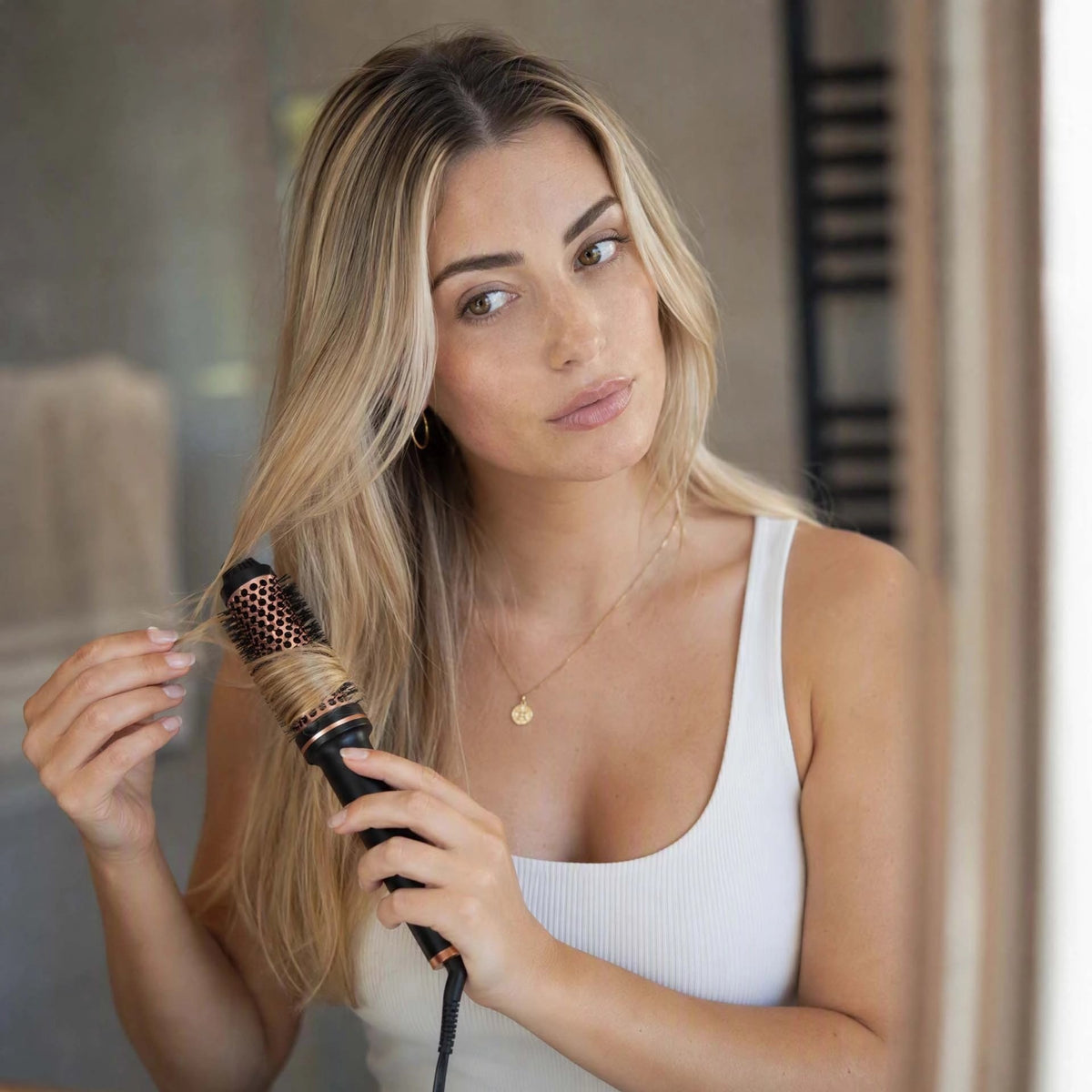 Brosse chauffante femme aux longs cheveux blonds qui coiffe ses cheveux 