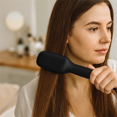 Jeune femme aux longs cheveux bruns qui se coiffe avec la brosse chauffante lissante