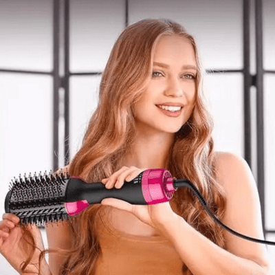 Jeune femme cheveux longs châtains qui se coiffe avec la brosse chauffante à air chaud de couleur noir et rose