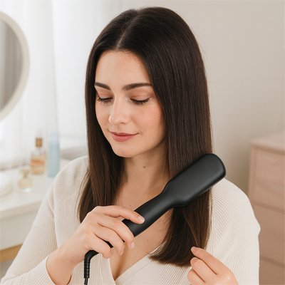 Jeune femme aux longs cheveux bruns qui se coiffe avec la brosse chauffante lissante