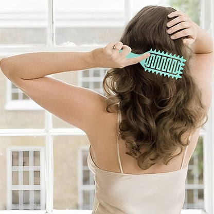 Jeune femme aux longs cheveux bruns vue de dos qui coiffe ses cheveux avec la brosse cheveux bouclés de couleur verte