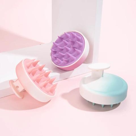 brosse cheveux massage trois couleurs posées sur un plan rose et blanc