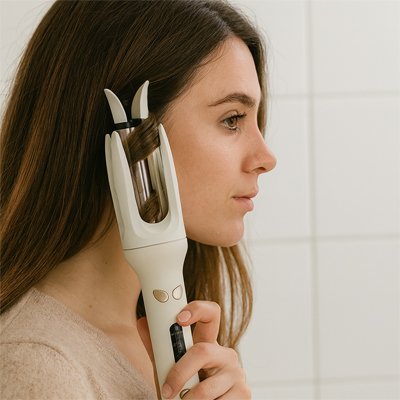 jeune femme qui utilise le fer bouclant pour boucler ses cheveux longs