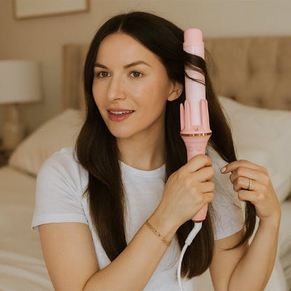 Jeune femme de 20-25 ans aux longs cheveux bruns qui se coiffe avec le fer bouclant de couleur rose