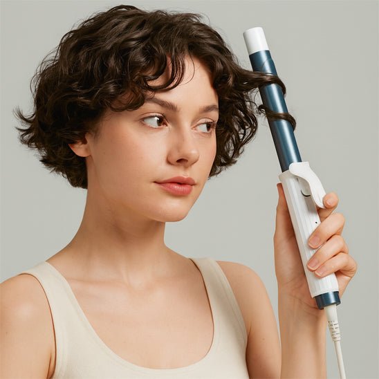 Jeune femme mi vingtaine qui se coiffe les cheveux avec le fer bouclant 