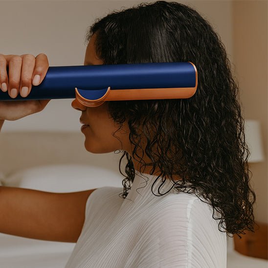 Jeune femme aux longs cheveux bouclés noirs qui se coiffe avec le fer bouclant de couleur bleue