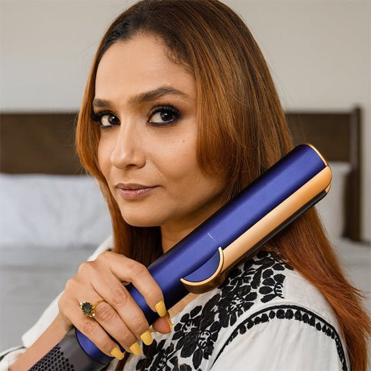 Jeune femme aux longs cheveux roux qui se coiffe avec le fer bouclant de couleur bleue